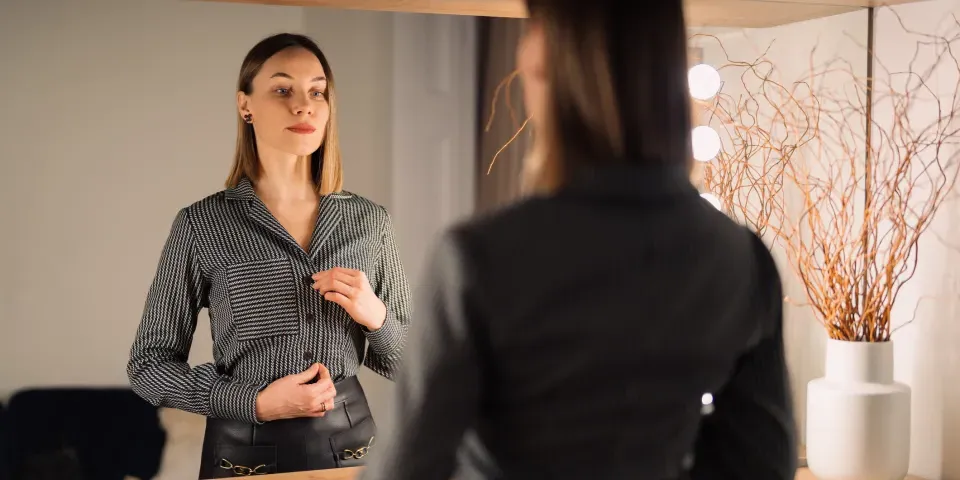 Self-confident woman looking at her reflection into the mirror indoors.